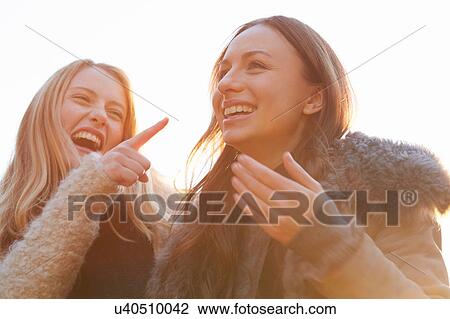 Stock Image - Two female friends, walking outdoors, laughing. Fotosearch
