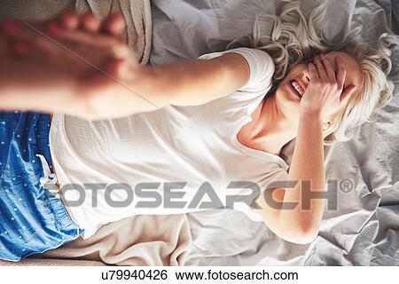 Stock Photograph - Woman lying on bed, man pulling her off bed, elevated view. Fotosearch