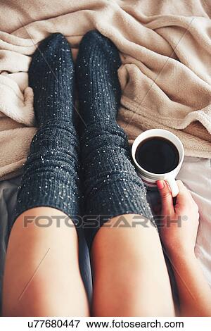Woman sitting on bed, wearing warm socks, holding cup of coffee, low section, overhead view View Large Photo Image Stock Photo - Woman sitting on bed, wearing warm socks, holding cup of coffee, low section, overhead view. Fotosearch