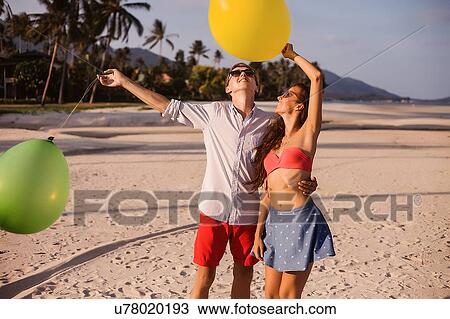 Stock Image - Young couple on beach looking up at balloons, Koh Samui, Thailand. Fotosearch