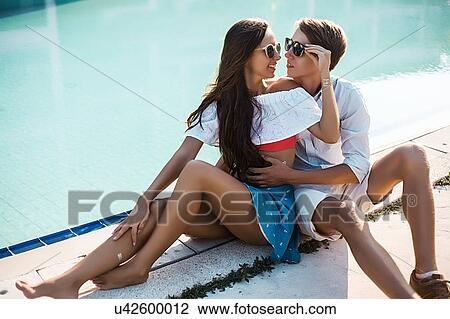 Stock Image - Young couple sitting on poolside, Koh Samui, Thailand. Fotosearch