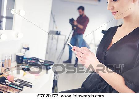 Young female model looking at smartphone before photo shoot View Large Photo Image Stock Image - Young female model looking at smartphone before photo shoot. Fotosearch
