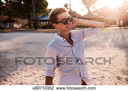 Stock Image - Young man with hand on ear at beach, Koh Samui, Thailand. Fotosearch