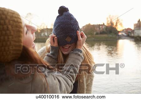 Young woman putting knitted hat on friend, hat covering eyes, laughing View Large Photo Image Stock Photograph - Young woman putting knitted hat on friend, hat covering eyes, laughing. Fotosearch