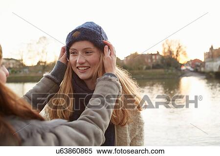 Young woman putting knitted hat on friend, outdoors, smiling View Large Photo Image Stock Photography - Young woman putting knitted hat on friend, outdoors, smiling. Fotosearch