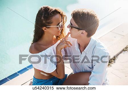 Stock Photography - Young woman with finger on boyfriend's lips at poolside, Koh Samui, Thailand. Fotosearch
