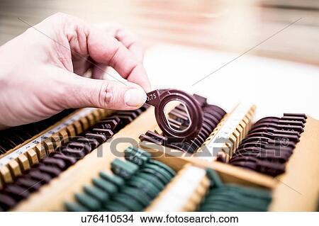 Picture - Close-up of hand holding lens from rack, used for eye test.. Fotosearch