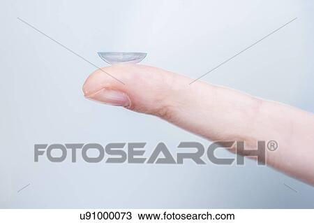 Stock Image - Close-up of person holding contact lens on finger.. Fotosearch