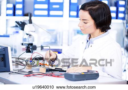 Stock Image - Female engineer soldering a circuit board. Fotosearch