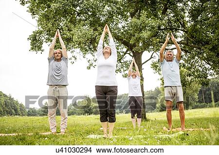 Picture - Four people doing yoga in field. Fotosearch