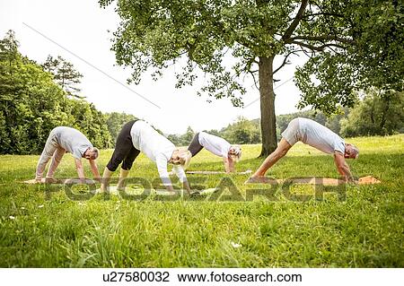 Stock Image - Four people doing yoga in field. Fotosearch