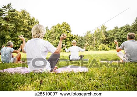Stock Photo - Four people doing yoga in field. Fotosearch