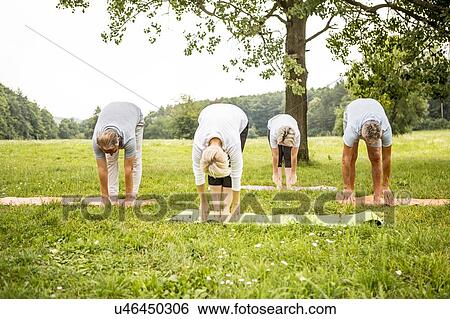 Stock Photograph - Four people doing yoga in field. Fotosearch
