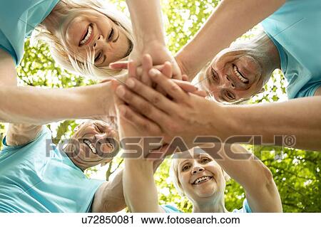 Stock Image - Four people in group huddle, low angle view. Fotosearch