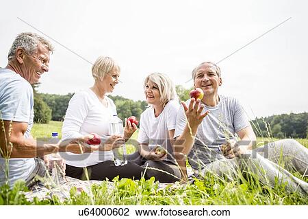Stock Image - Four people sitting on grass with apples. Fotosearch