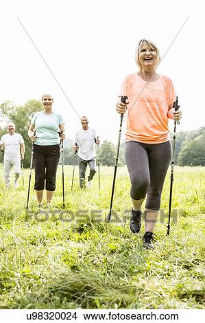 Picture - Four people walking in grass with walking poles. Fotosearch
