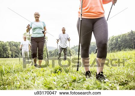 Stock Photo - Four people walking in grass with walking poles. Fotosearch