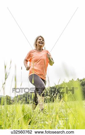 Stock Image - Mature woman jogging in grass. Fotosearch