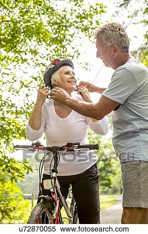 Stock Photography - Mature woman on bike, Man assisting with helmet. Fotosearch