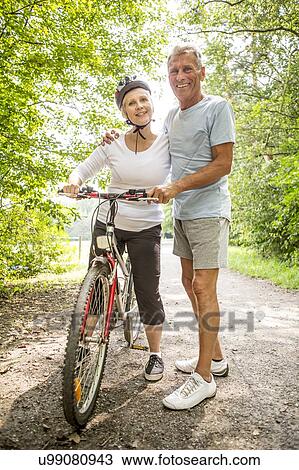 Stock Image - Mature woman on bike, Man with arm around. Fotosearch