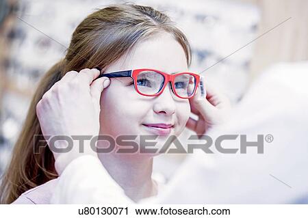 Stock Image - Optometrist trying glasses on girl. Fotosearch