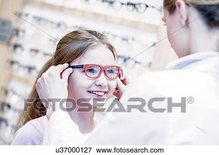 Optometrist trying glasses on girl View Large Photo Image Stock Photo - Optometrist trying glasses on girl. Fotosearch