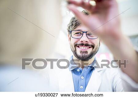 Stock Photo - Optometrist trying glasses on woman. Fotosearch
