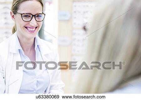 Optometrist trying glasses on woman View Large Photo Image Stock Photo - Optometrist trying glasses on woman. Fotosearch