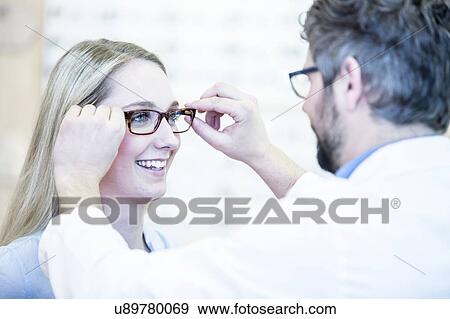 Stock Photo - Optometrist trying glasses on woman. Fotosearch