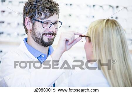 Stock Photography - Optometrist trying glasses on woman. Fotosearch