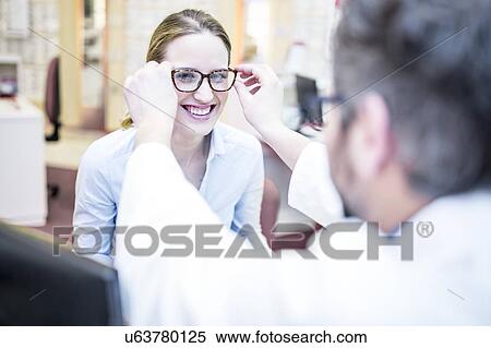 Optometrist trying glasses on woman View Large Photo Image Stock Photography - Optometrist trying glasses on woman. Fotosearch
