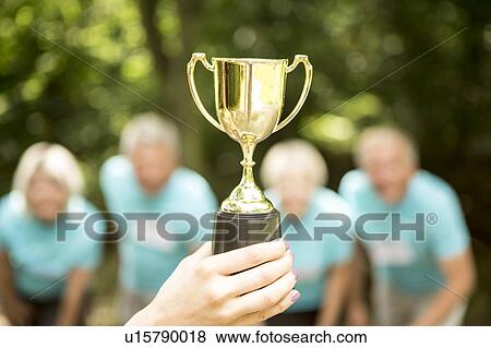 Stock Photo - Person holding trophy with people in background. Fotosearch