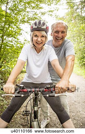 Stock Photograph - Senior woman on bike, mature man assisting. Fotosearch