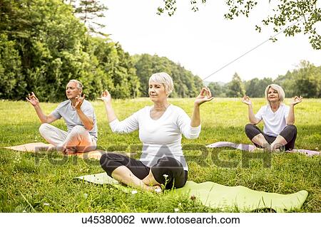 Stock Image - Three people doing yoga in field. Fotosearch