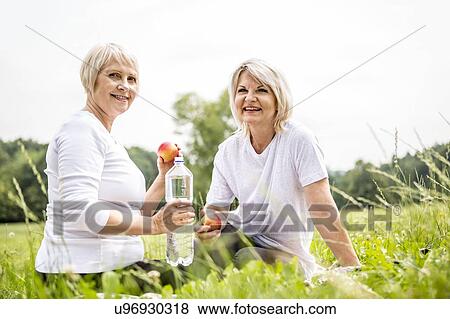 Two women sitting on grass with apples and water View Large Photo Image Stock Photo - Two women sitting on grass with apples and water. Fotosearch