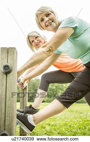 Stock Photo - Two women smiling towards camera with legs on railings. Fotosearch