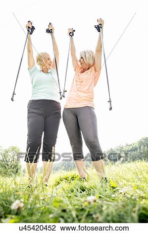 Two women with walking poles raised in air View Large Photo Image Stock Image - Two women with walking poles raised in air. Fotosearch