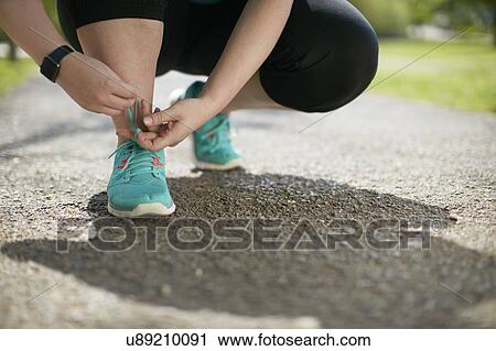 Stock Image - Woman crouching, tying up trainers. Fotosearch