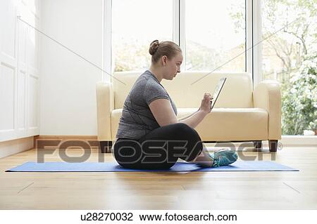 Stock Image - Woman sitting on floor using digital tablet. Fotosearch