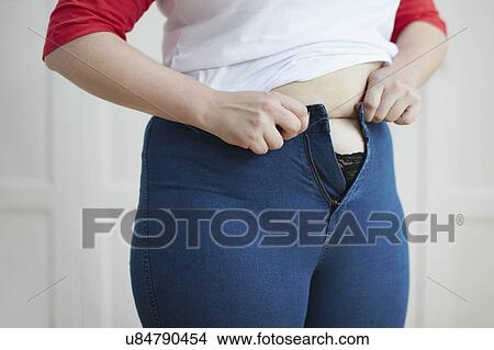 Picture - Woman trying to button jeans over tummy. Fotosearch