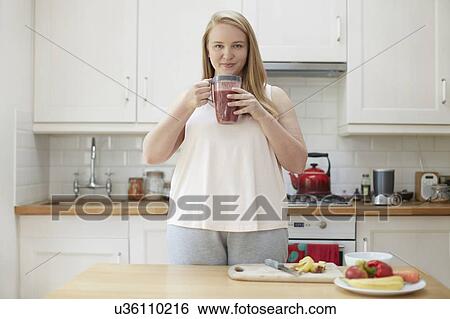 Young woman drinking smoothie in kitchen View Large Photo Image Stock Photograph - Young woman drinking smoothie in kitchen. Fotosearch