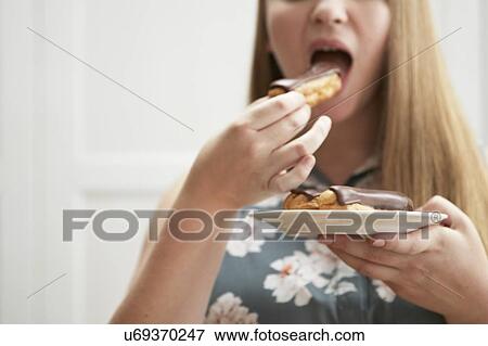 Stock Photo - Young woman eating chocolate eclair. Fotosearch