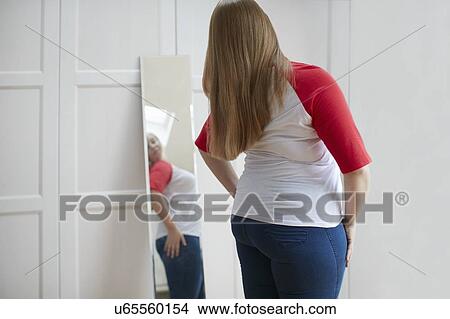 Picture - Young woman looking at reflection in mirror. Fotosearch