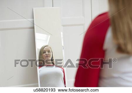 Stock Image - Young woman looking at reflection in mirror. Fotosearch