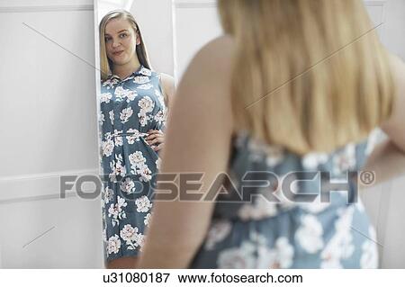 Stock Photo - Young woman looking at reflection in mirror, smiling. Fotosearch