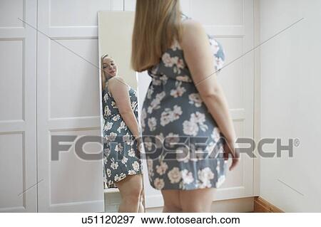 Stock Photo - Young woman looking at reflection in mirror. Fotosearch