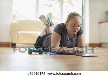 Stock Photography - Young woman lying on yoga mat using digital tablet. Fotosearch