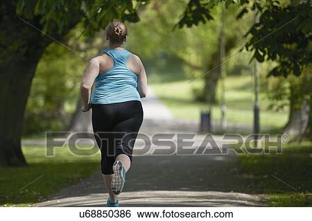 Stock Photograph - Young woman running on path, rear view. Fotosearch