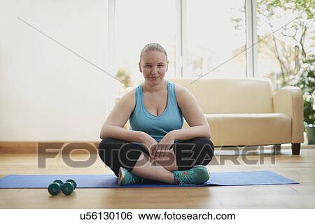 Stock Photograph - Young woman sitting cross legged on yoga mat. Fotosearch