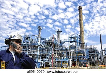 Stock Image - Industrial worker on oil and gas refinery using cell phone. Fotosearch